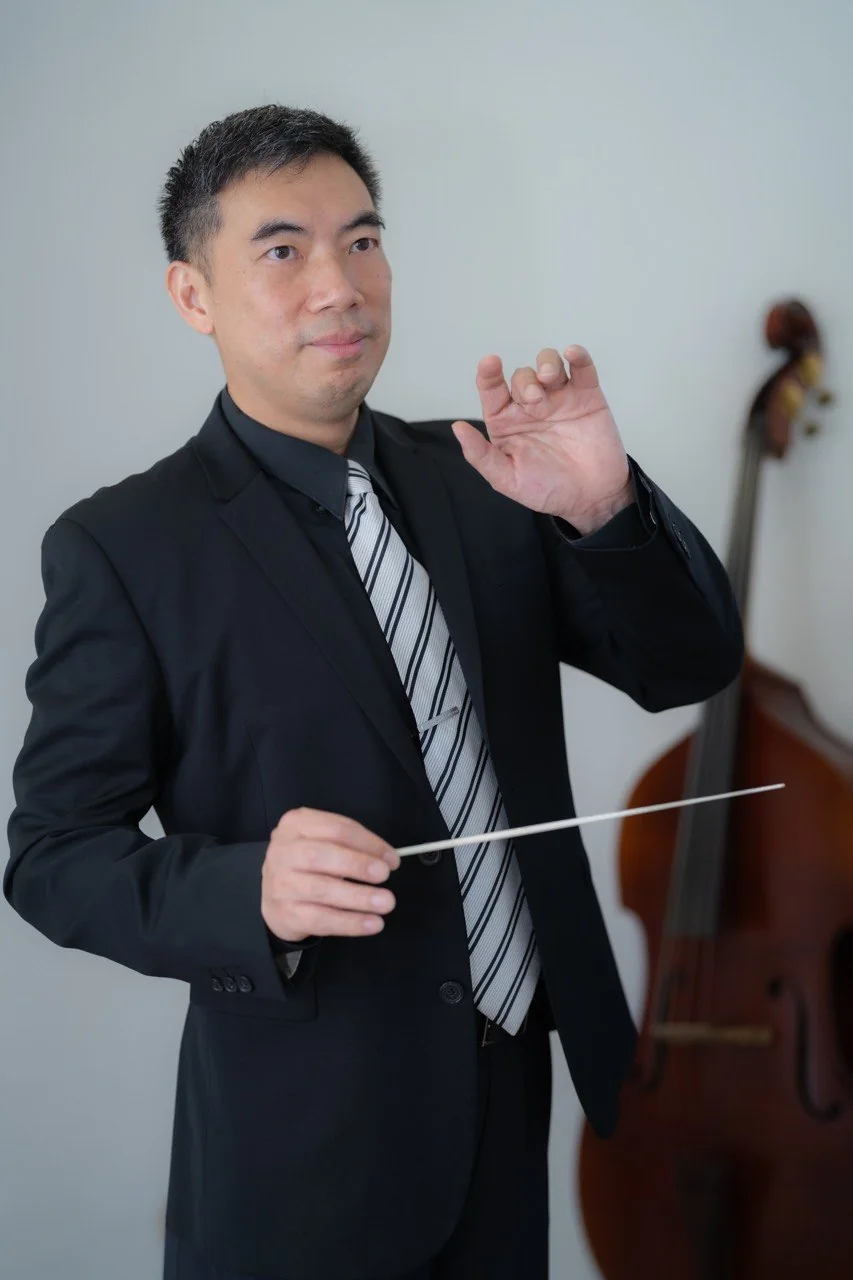 Amos Lee in black suit and tie, holding a baton mid-gesture